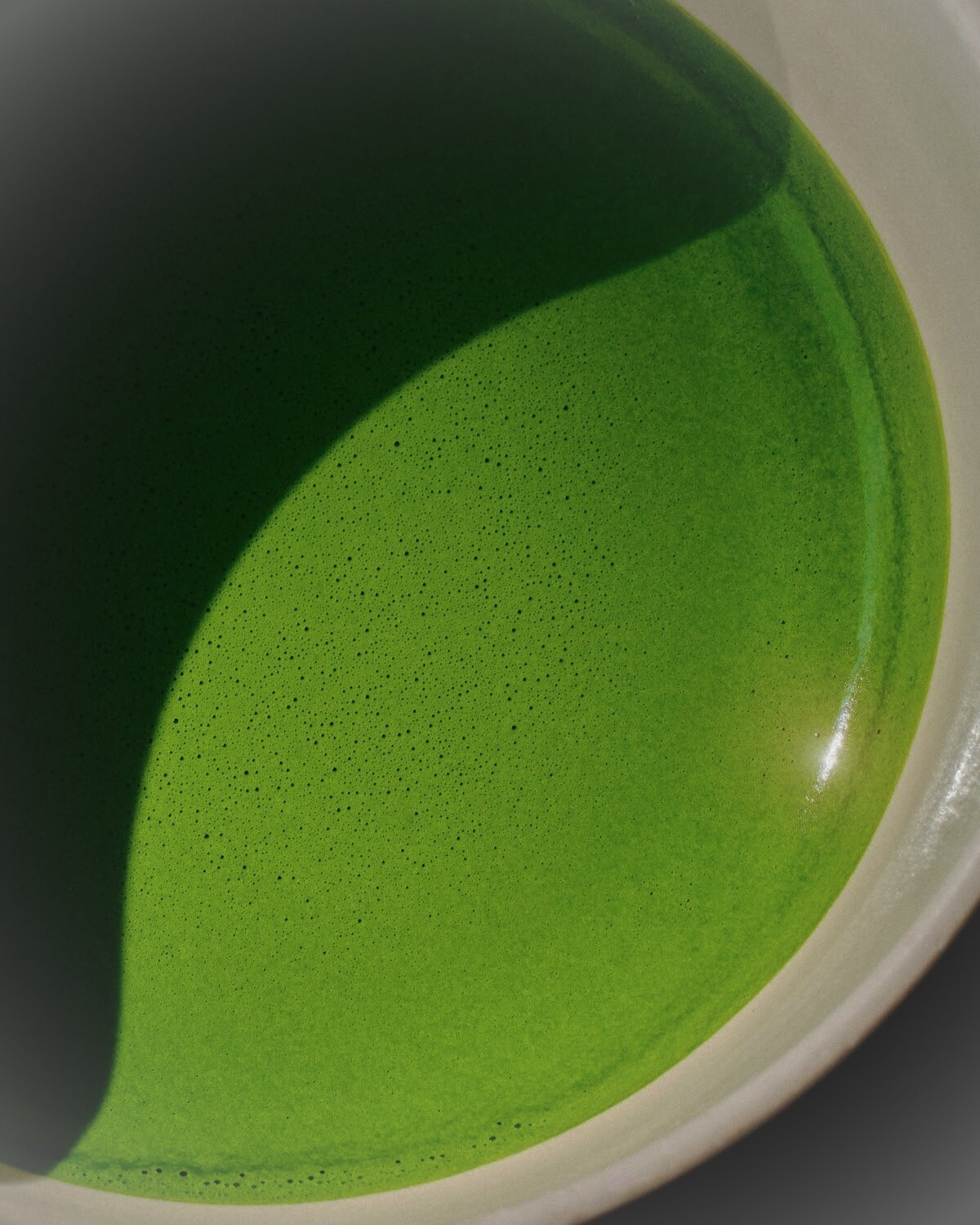 A close-up of freshly whisked matcha — vibrant jade foam against the curve of a ceramic chawan.